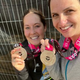 Two women standing together holding their medals after completing a fundraising event