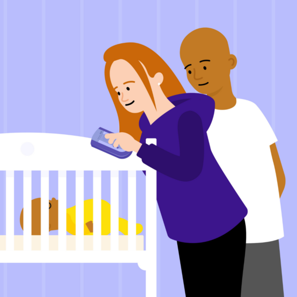 Parents standing beside baby in a cot holding a baby monitor