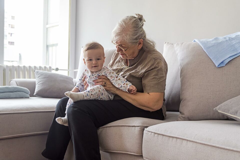 Grandmother sitting on a sofa with a baby on her lap wearing a baby grow.