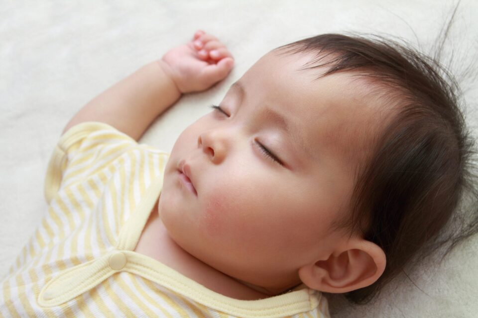 Close up of a baby's face, sleeping on their back and wearing a yellow stripy baby grow.