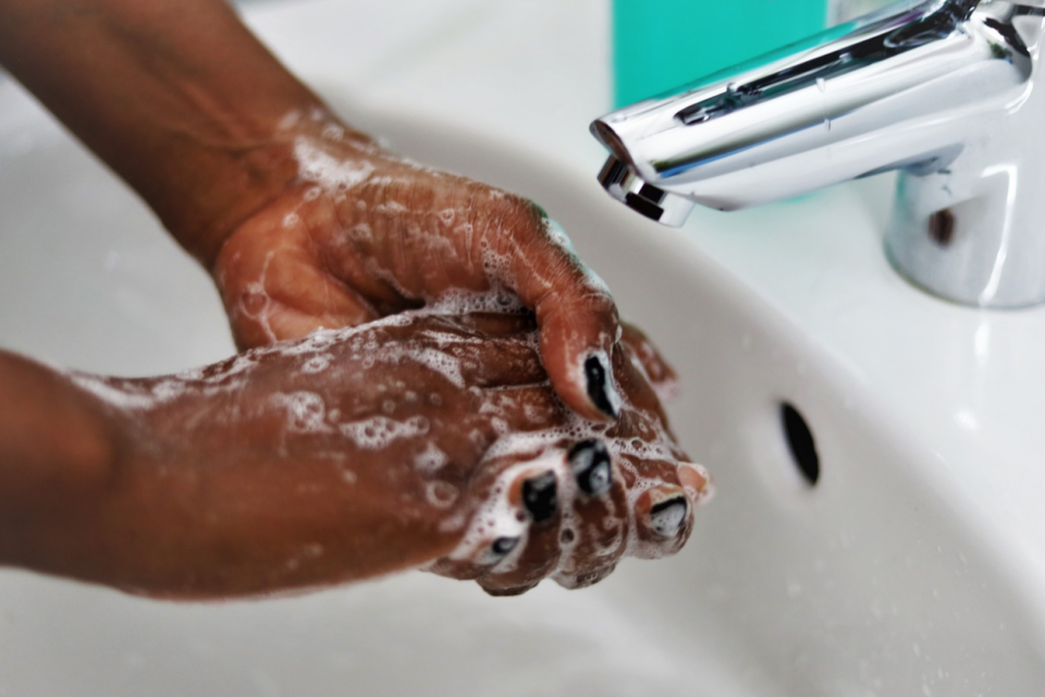 A close up of a woman washing her hands. She has soap suds on her hands and black nail polish, and the tap is off.