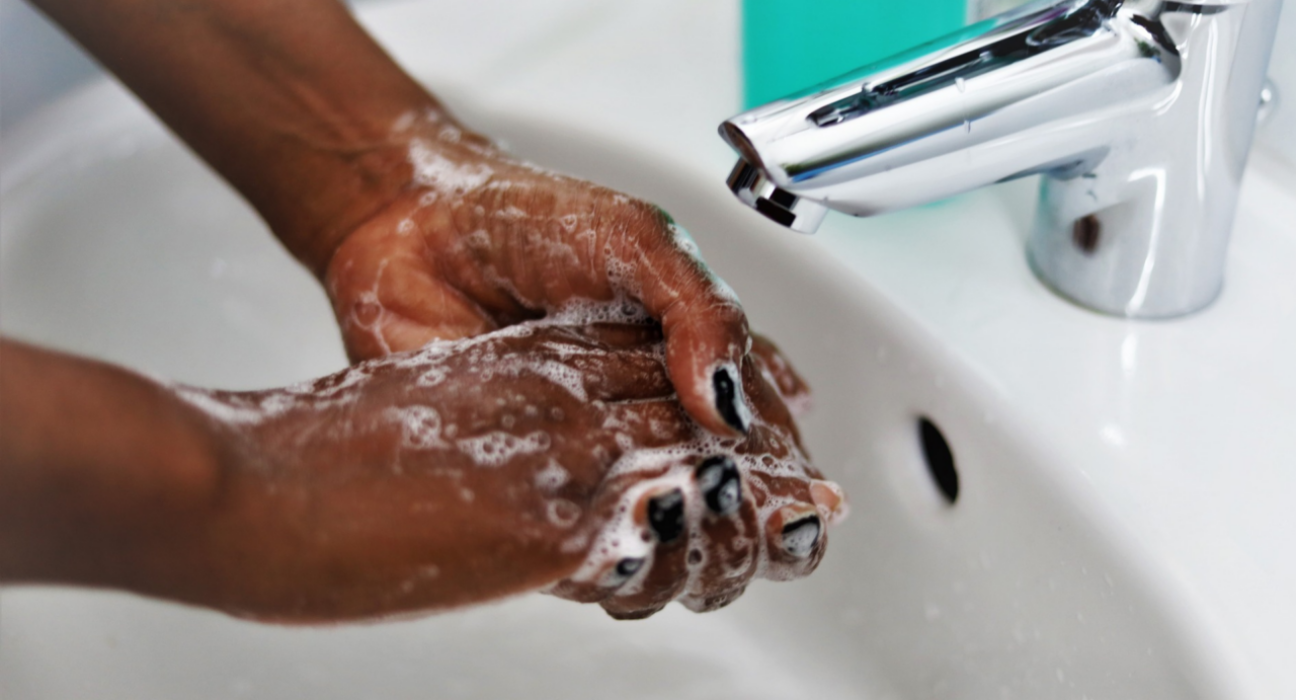 A close up of a woman washing her hands. She has soap suds on her hands and black nail polish, and the tap is off.