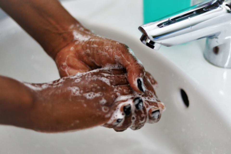 A close up of a woman washing her hands. She has soap suds on her hands and black nail polish, and the tap is off.