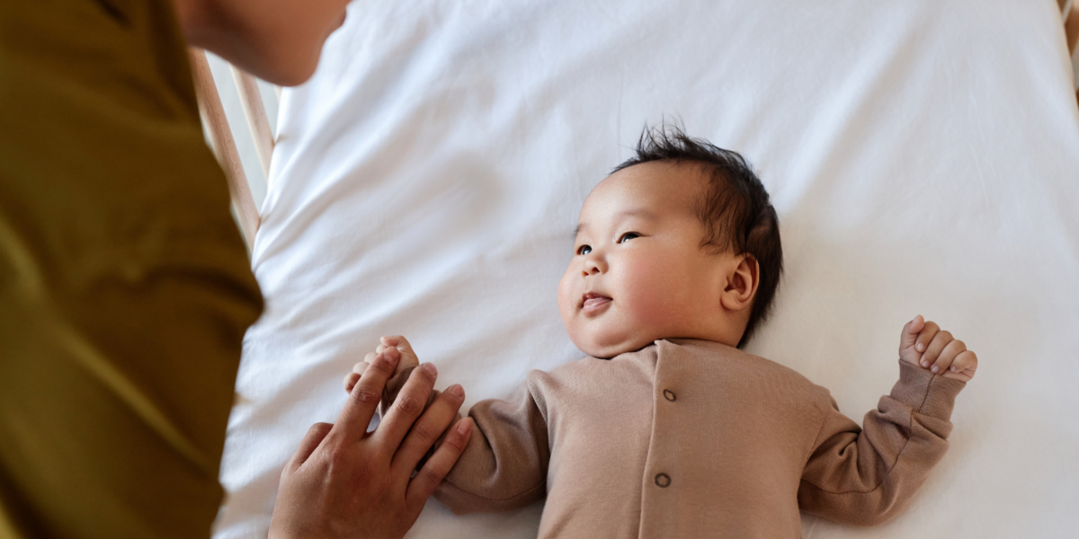 A baby is being put down to sleep in a cot. They are looking up at their parent.