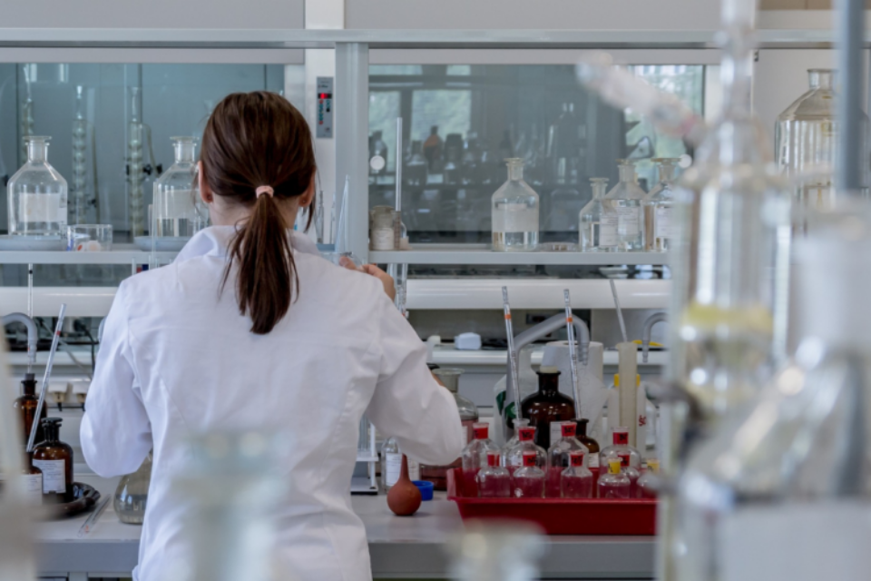 A researcher from the back, seemingly organising lab samples, wearing a lab coat with her hair tied back.
