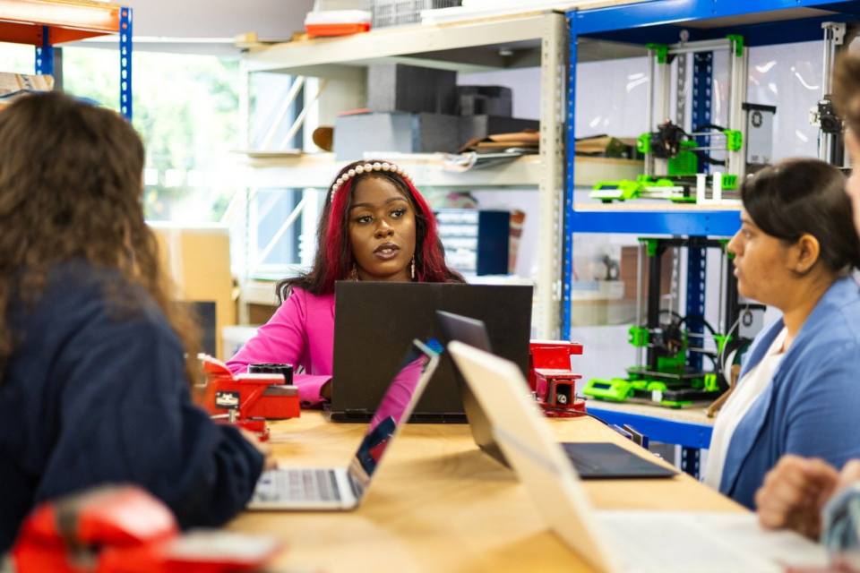 A woman is talking to a group of people in a meeting, they all have their laptops open.