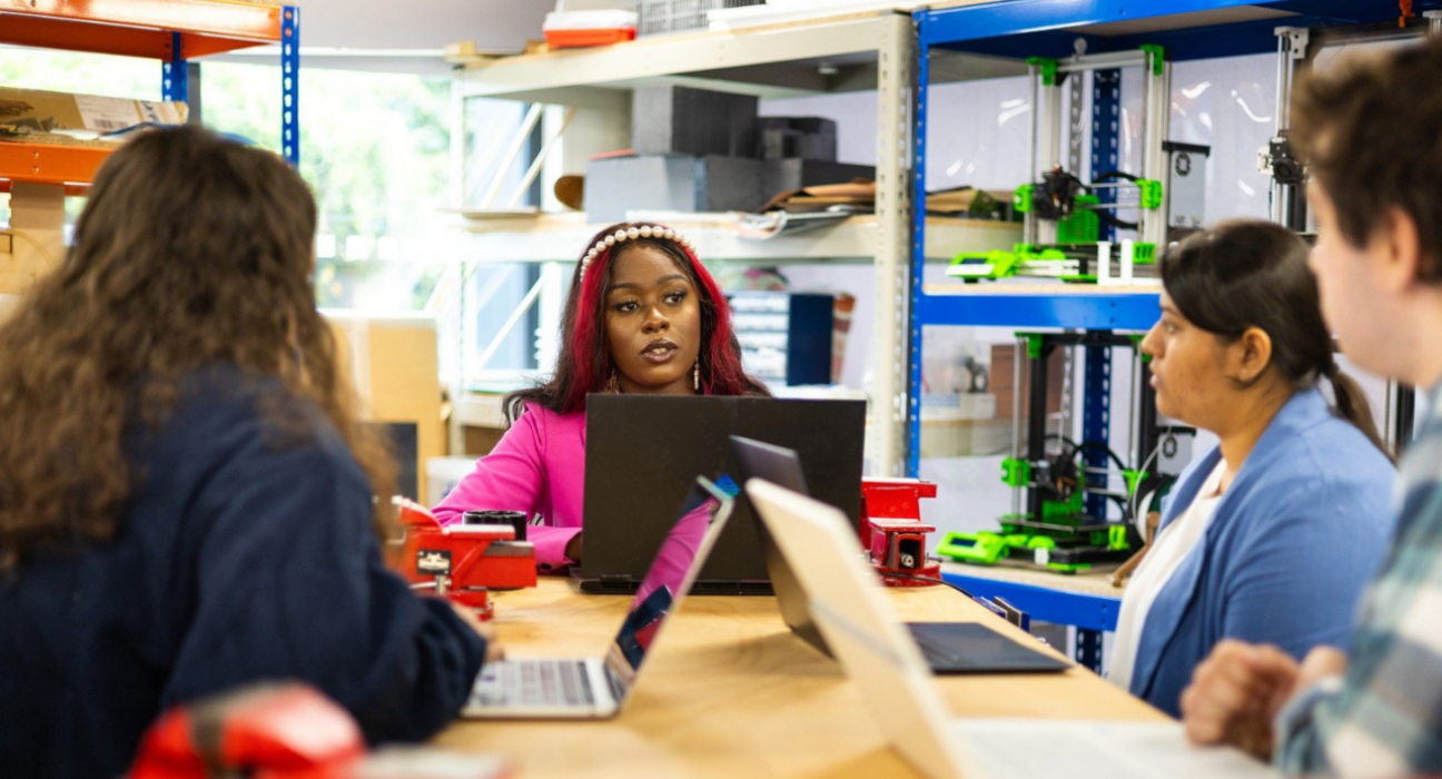 A woman is talking to a group of people in a meeting, they all have their laptops open.