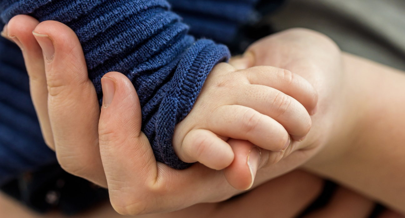 A close up of a baby's hand grasping the parent's hand