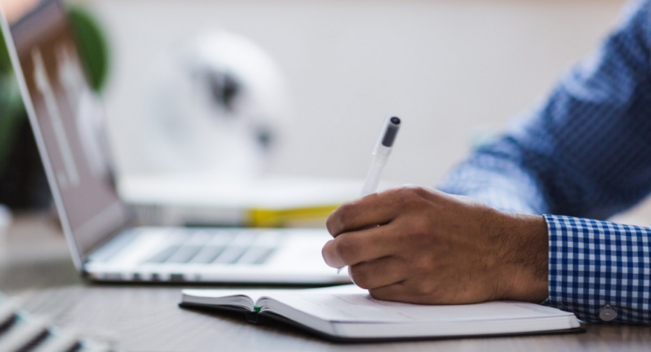 Close-up of a researcher making notes in a notebook. They have a laptop to the side of them.