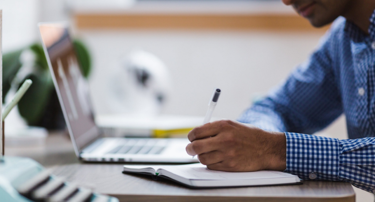 Close-up of a researcher making notes in a notebook. They have a laptop to the side of them.