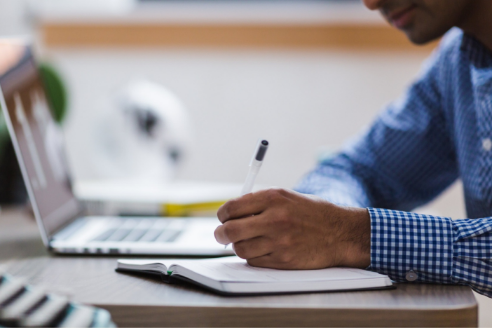 Close-up of a researcher making notes in a notebook. They have a laptop to the side of them.