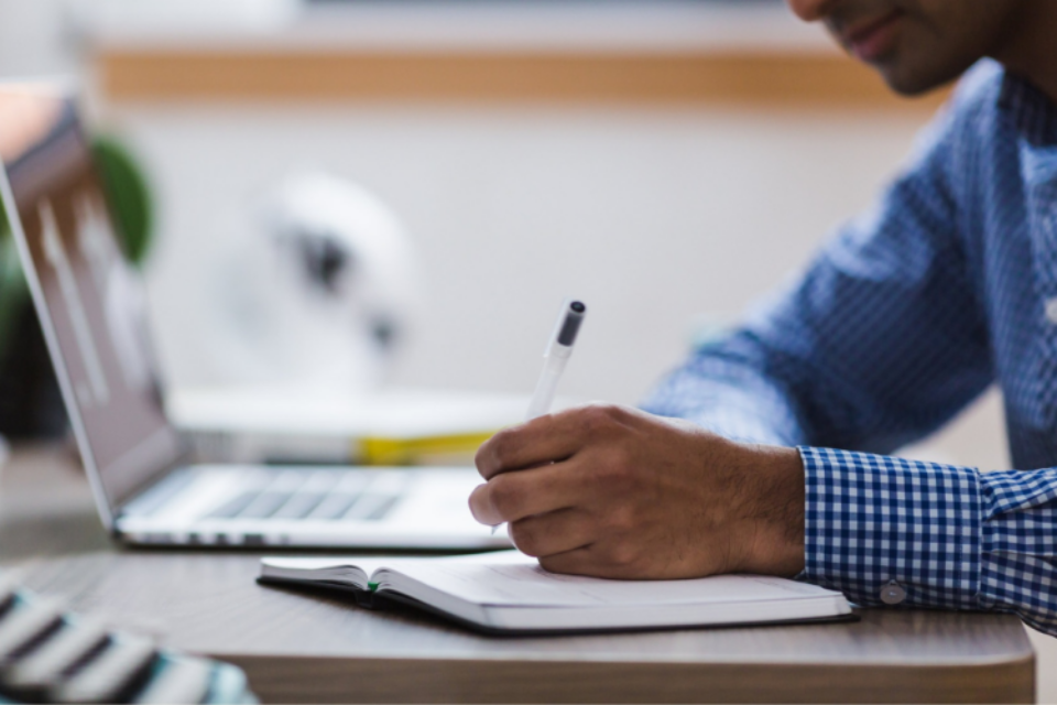 Close-up of a researcher making notes in a notebook. They have a laptop to the side of them.