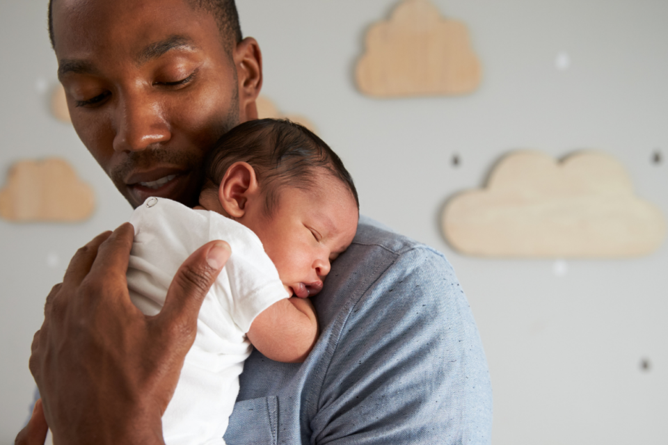 A dad is holding a very young baby on his shoulder. His hand is caressing the baby's back, and he's looking down at the baby.