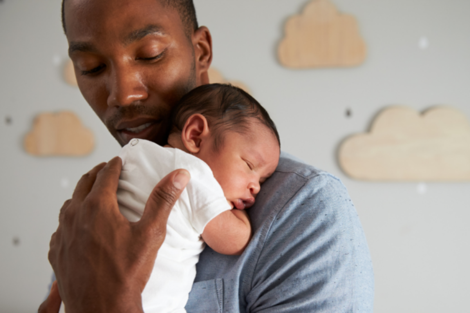 A dad is holding a very young baby on his shoulder. His hand is caressing the baby's back, and he's looking down at the baby.