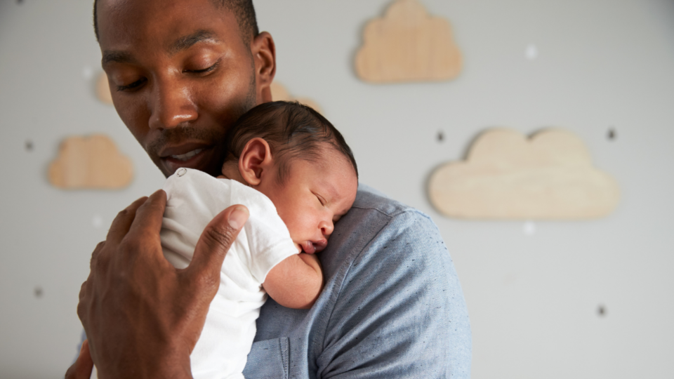A dad is holding a very young baby on his shoulder. His hand is caressing the baby's back, and he's looking down at the baby.