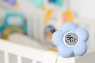 A thermometer, shaped as a flower, sits on a baby's cot.