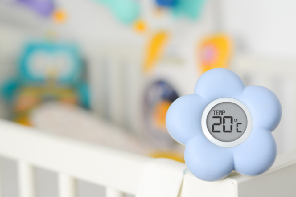 A thermometer, shaped as a flower, sits on a baby's cot.
