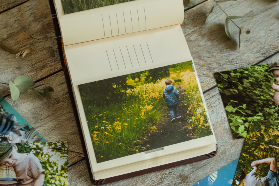 A photo album is open on the page of a little boy walking. He has his back to the camera, walking through forget-me-not flowers.