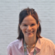 Alice wearing a pink shirt and a Lullaby lanyard, smiling at the camera in front of a white wall.