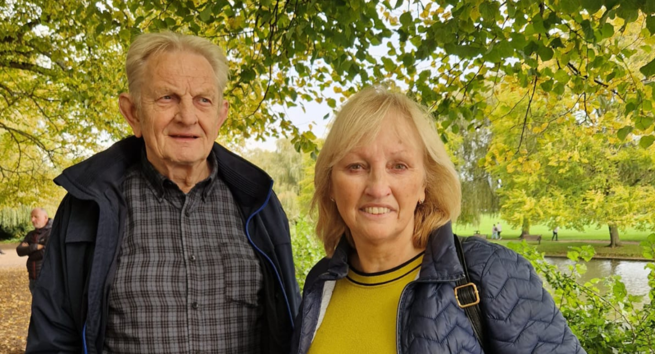 Bridget and Zbig are in a park surrounded by greenery. They are both smiling. Bridget is looking straight on, and Zbig to the side.