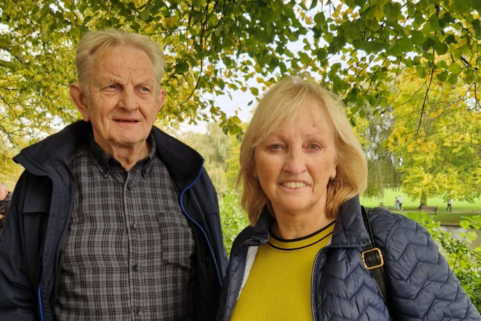 Bridget and Zbig are in a park surrounded by greenery. They are both smiling. Bridget is looking straight on, and Zbig to the side.