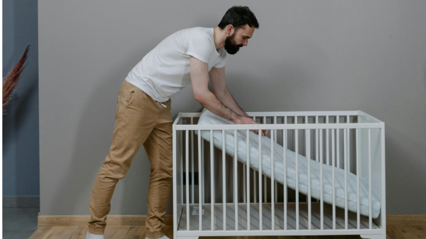 A parent is setting up the mattress in a cot. They are pushing the mattress onto the base of the cot.