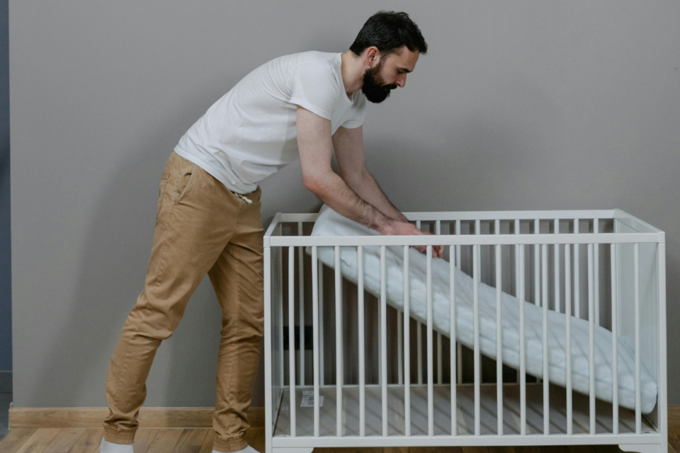 A parent is setting up the mattress in a cot. They are pushing the mattress onto the base of the cot.