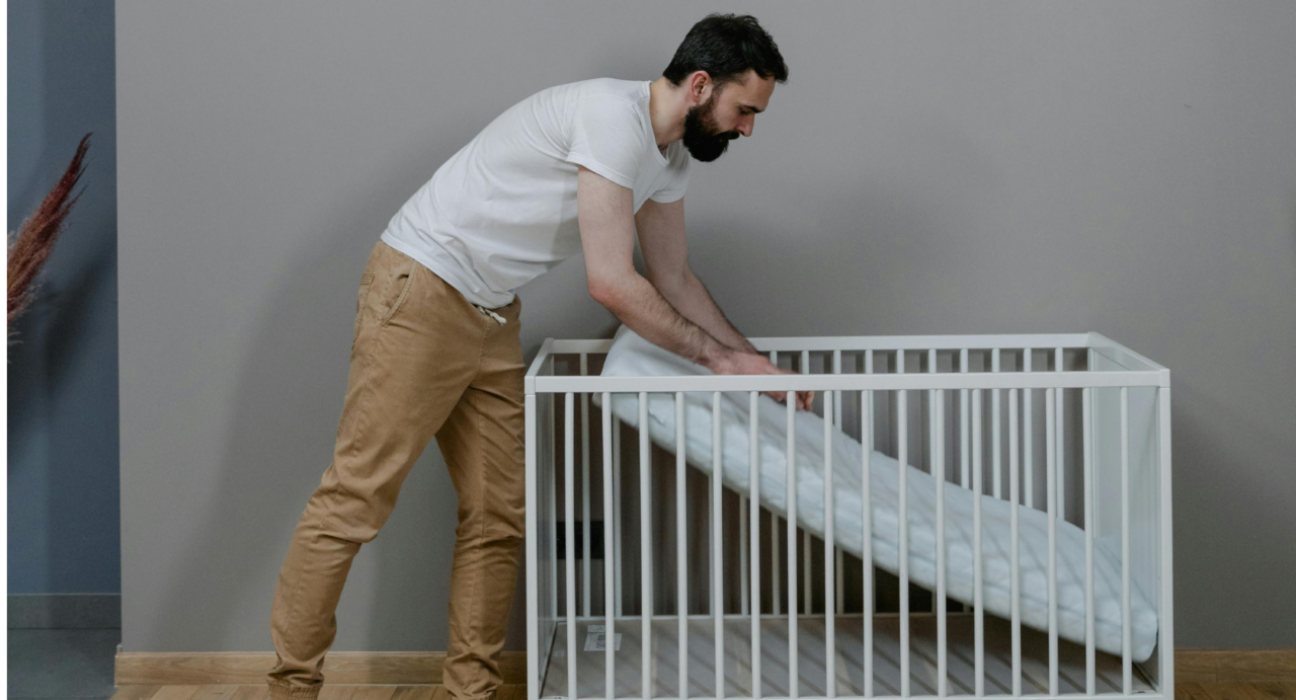 A parent is setting up the mattress in a cot. They are pushing the mattress onto the base of the cot.