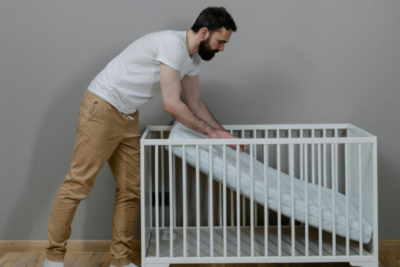 A parent is setting up the mattress in a cot. They are pushing the mattress onto the base of the cot.