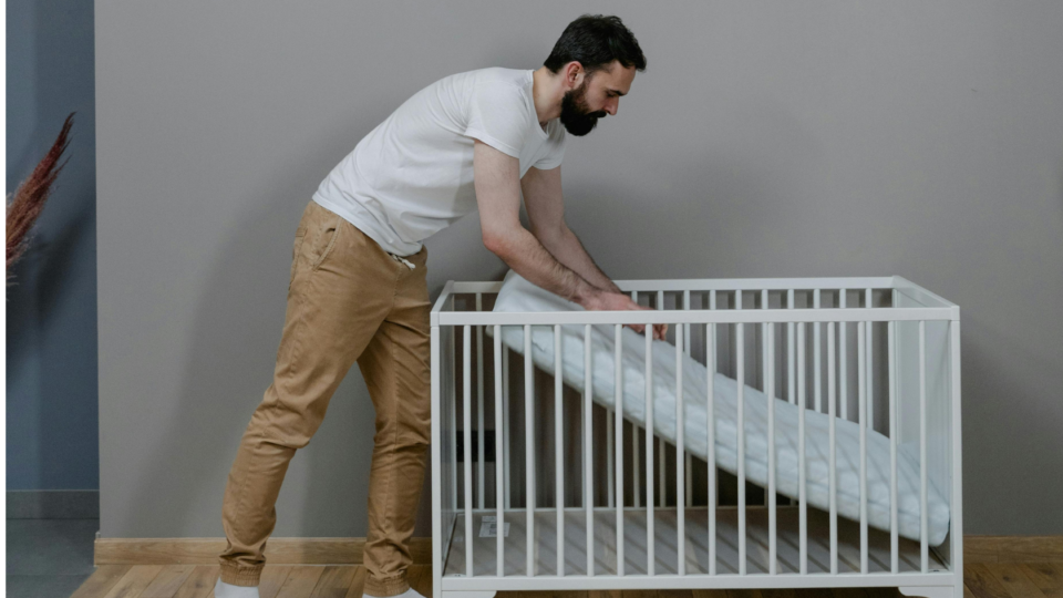 A parent is setting up the mattress in a cot. They are pushing the mattress onto the base of the cot.