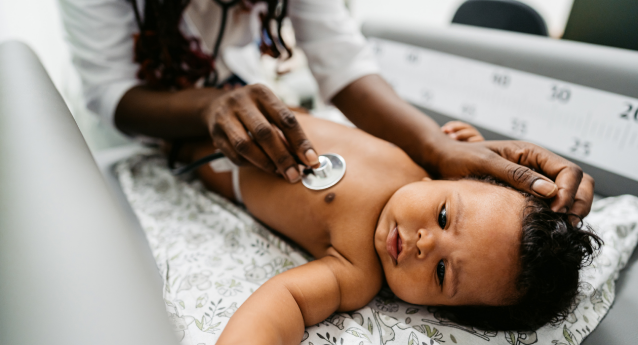 Baby lying on back as a doctor listens to their heart using a stethoscope.