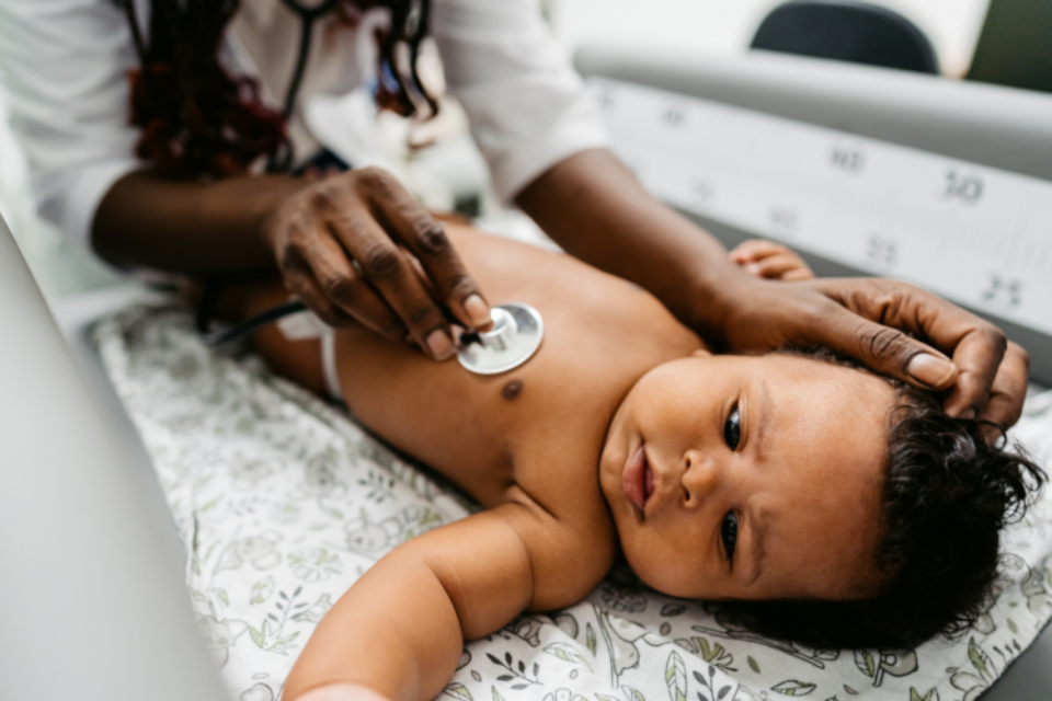 Baby lying on back as a doctor listens to their heart using a stethoscope.