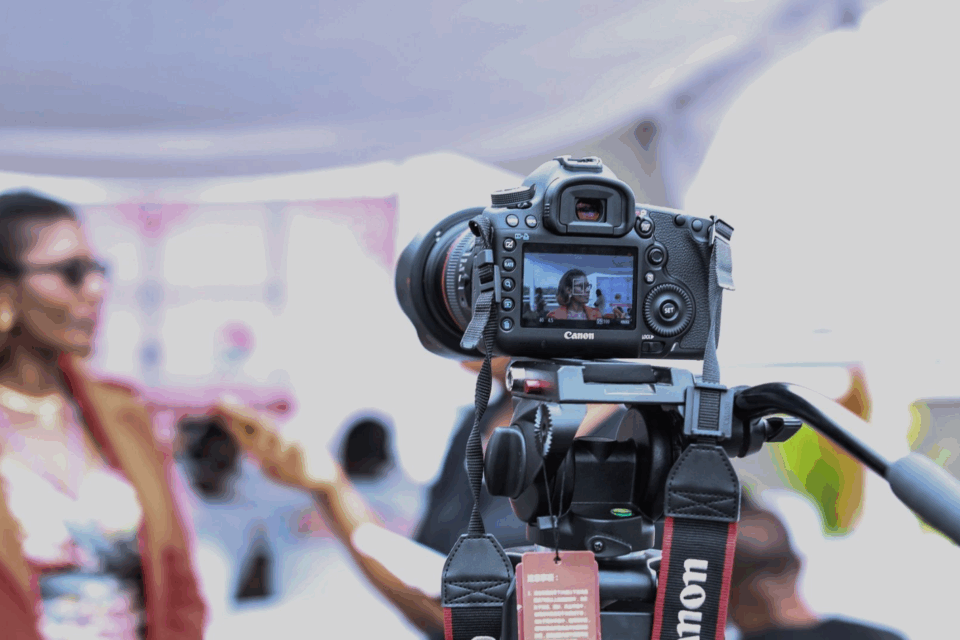 Camera on a tripod is filming a subject who is talking in the background to an interviewer out of screen.