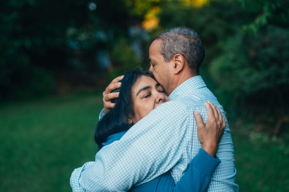 A man and a woman standing outside, hugging.