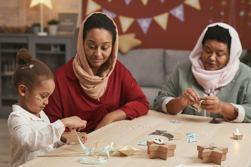 Two women and a child sitting at a table doing arts and crafts together.