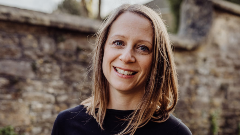 Portrait of Anna Pease wearing a black top, smiling at the camera in front of a brick wall.