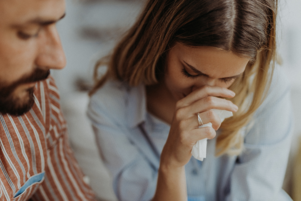 Upset lady with tissue in her hand looking down, with man sat beside her.