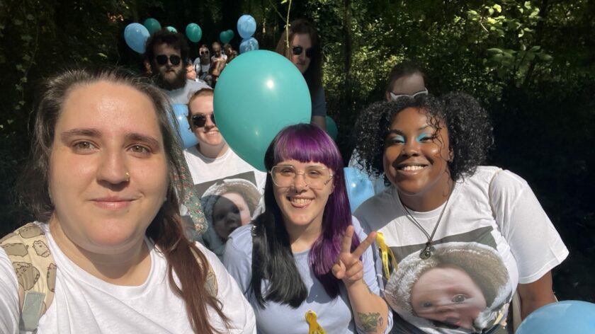 A group of fundraisers walking, smile at the camera. They are holding balloons and wearing yellow ribbons. They are wearing t-shirts with the baby's photo on.