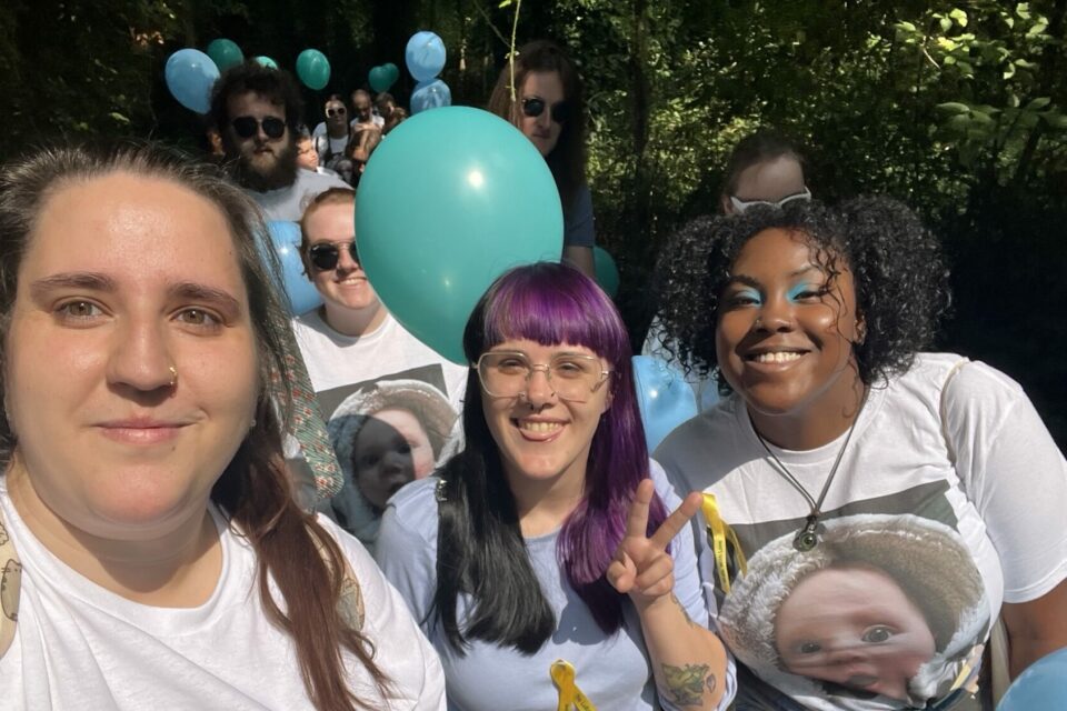 A group of fundraisers walking, smile at the camera. They are holding balloons and wearing yellow ribbons. They are wearing t-shirts with the baby's photo on.