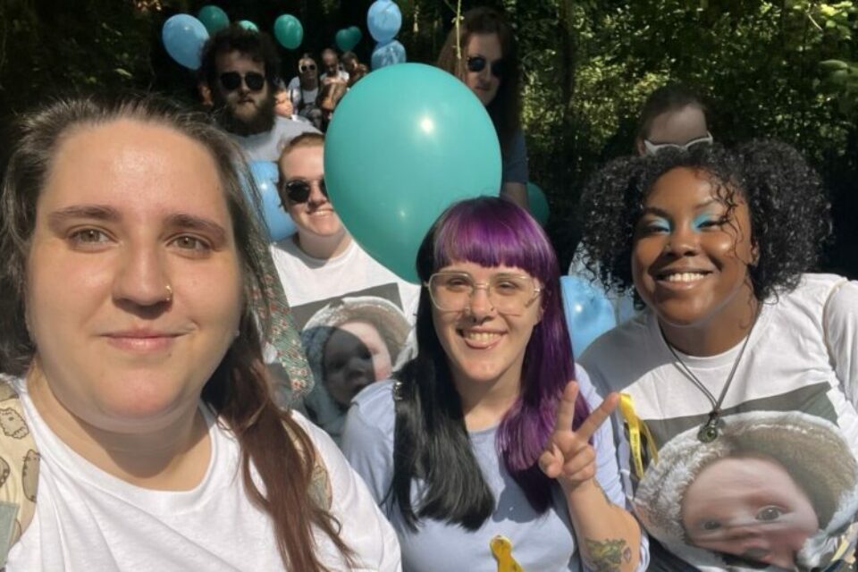 A group of fundraisers walking, smile at the camera. They are holding balloons and wearing yellow ribbons. They are wearing t-shirts with the baby's photo on.