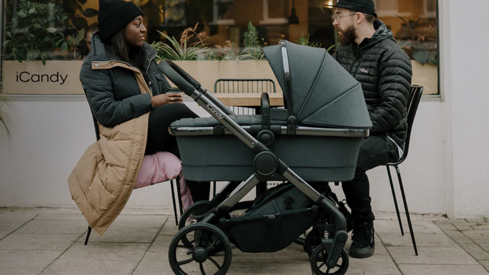 A man and woman drink coffee with a pushchair in front of them