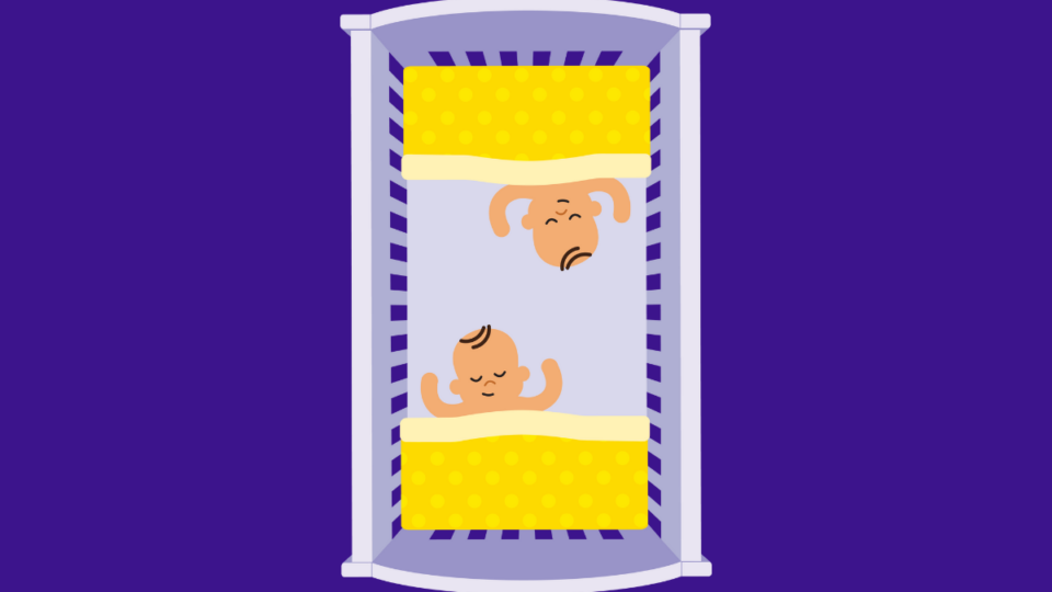 Twins are co-bedding in the same cot. Their heads are facing eachother with their feet to the foot of each end of the cot. They are sleeping and have a blanket tucked beneath their armpits.