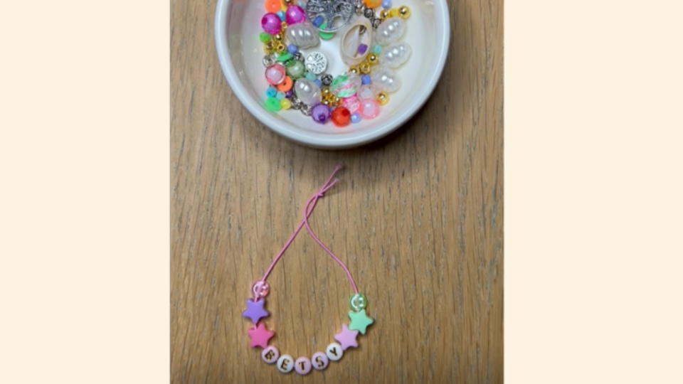Bracelet that says a child name, that has just been crafted. There is a bowl of beads above it.