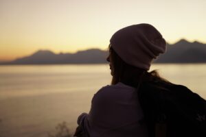 Lady wearing a beanie, outdoors looking out onto vast scenery.