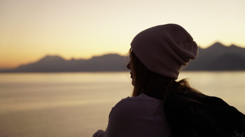 Lady wearing a beanie, outdoors looking out onto vast scenery.