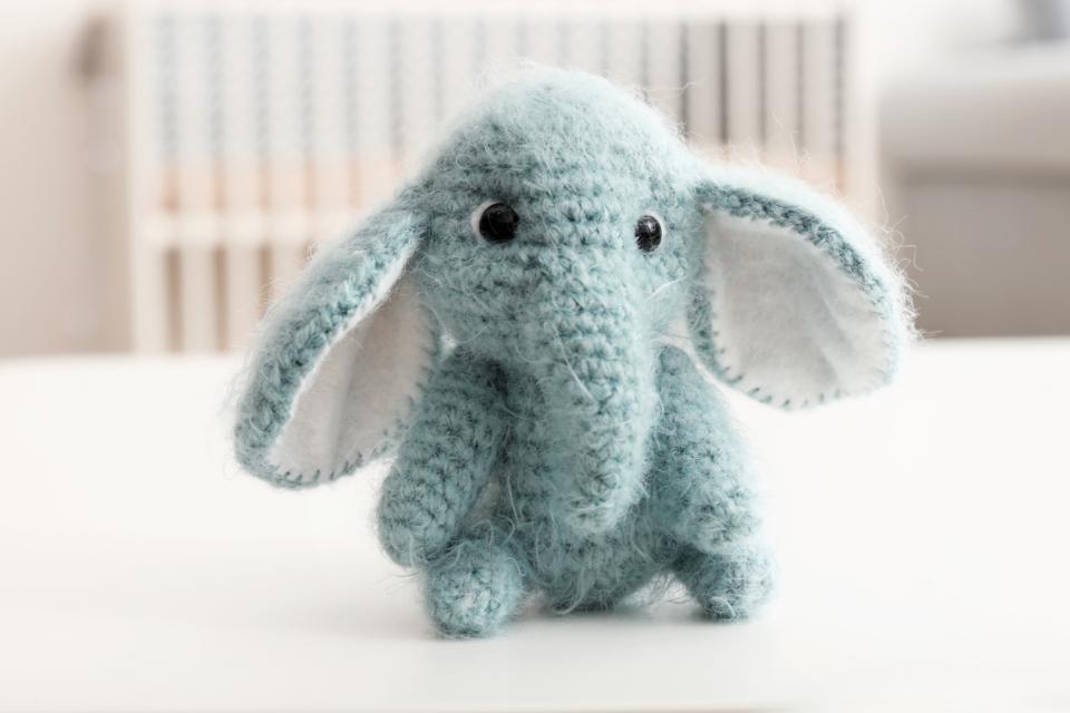 A crochet small baby toy elephant sits in front of a baby's crib