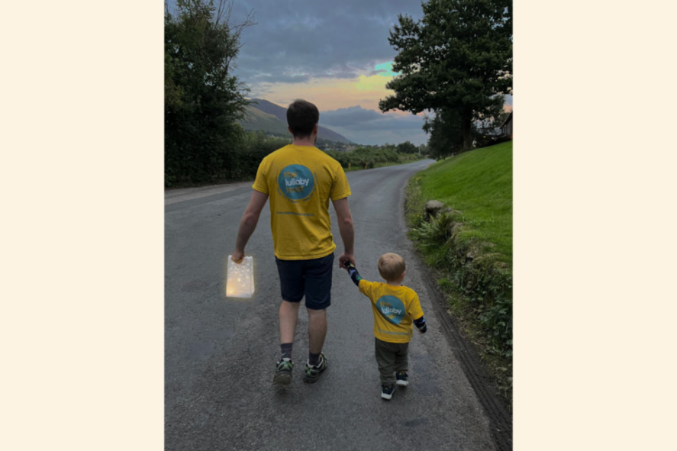 Matt and his son, Finn, are walking with their back to the camera. They are taking part in Little Stars Walk, with a lantern hanging from Matt's hand.