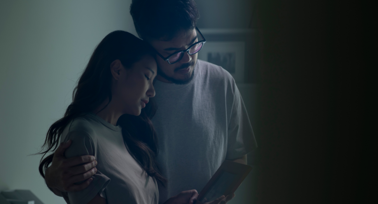 A man and woman are leaning into one another, looking upset at a photo frame that is out of view.