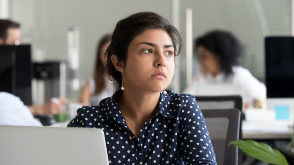 A woman is at work and is looking away from her laptop. She looks upset.