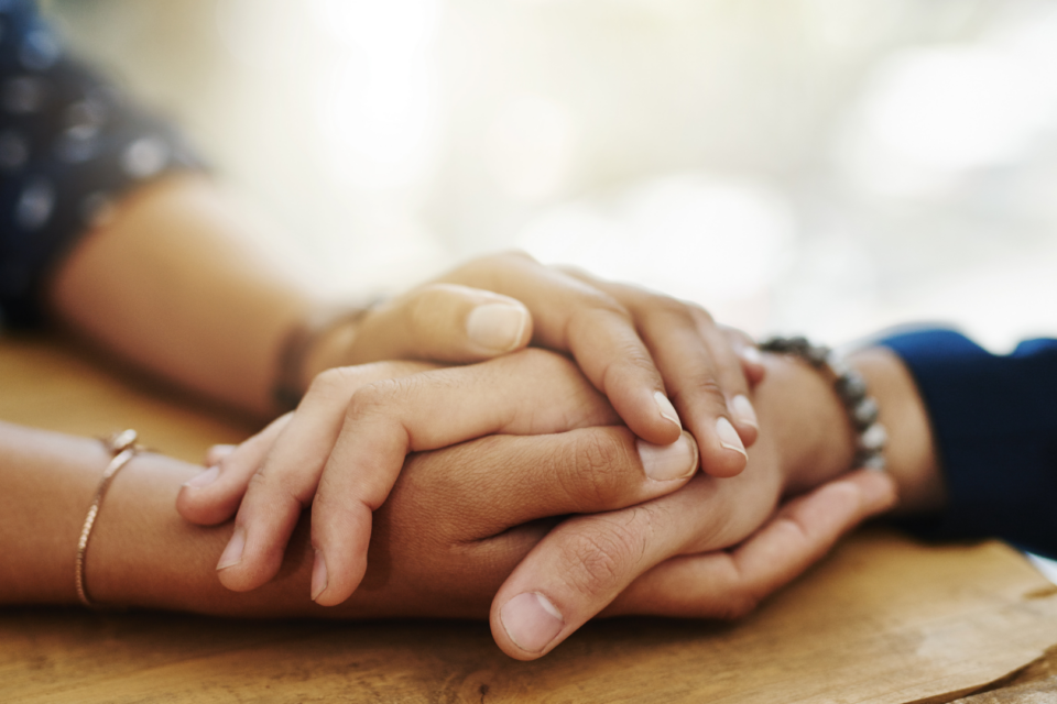 Two people are supporting one another by holding hands. They have light and medium light skin.